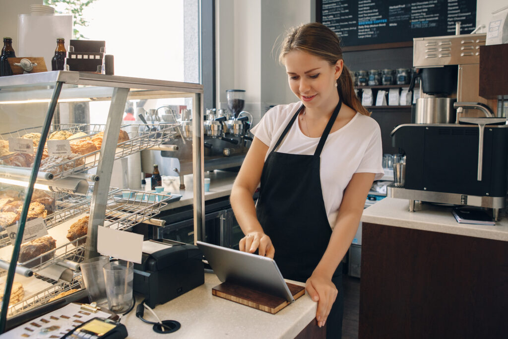 Kassiererin im Cafe tippt auf Tablet am Tresen